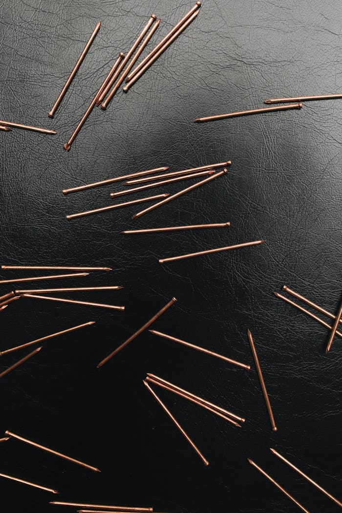 Artistic close-up of copper nails scattered on black leather background.